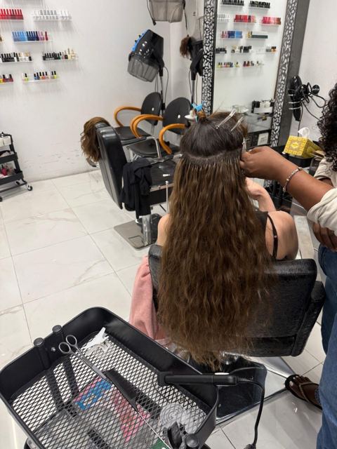 A stylist fitting long wavy hair extensions strand by strand at the salon